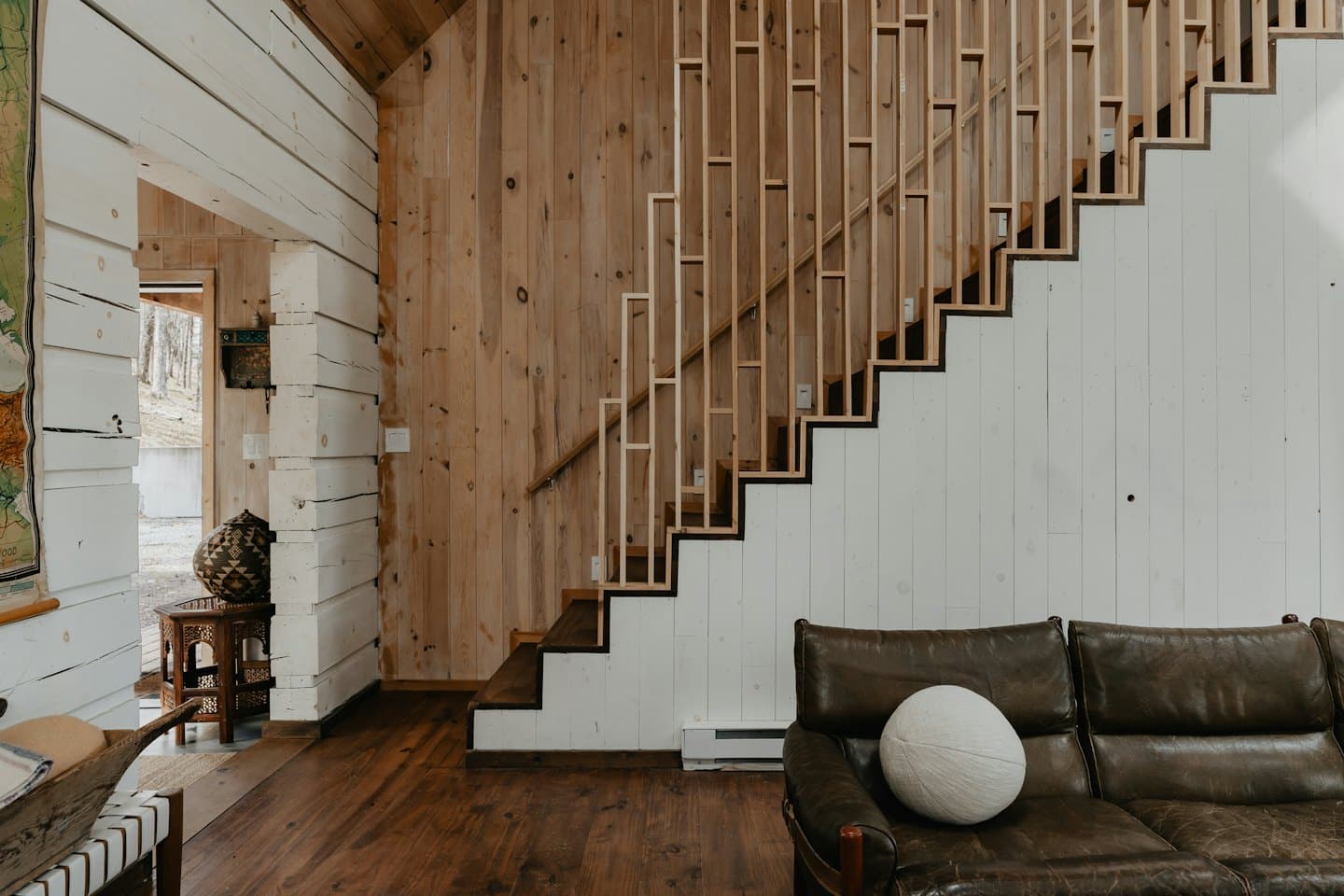 Living room with wood paneling, leather sofa, and wooden staircase.