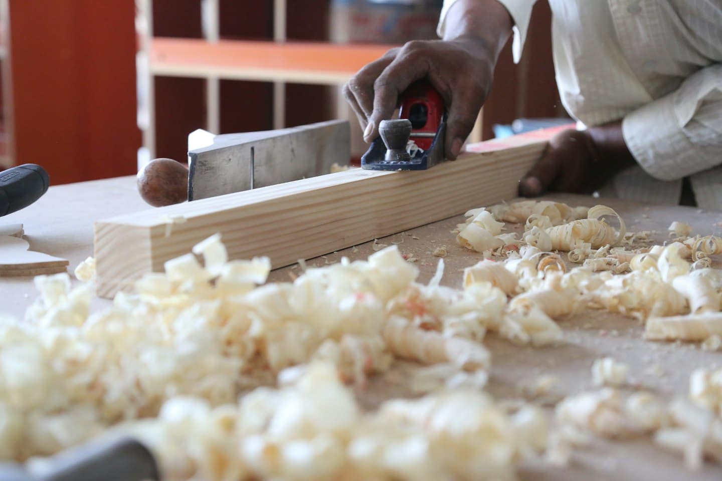 Hands use a hand plane to smooth a wooden plank.