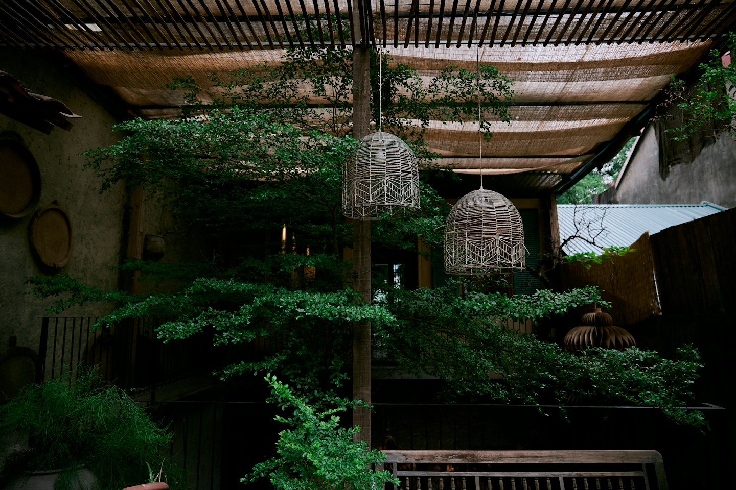 Woven pendant lamps hang above a wooden bench in a patio.