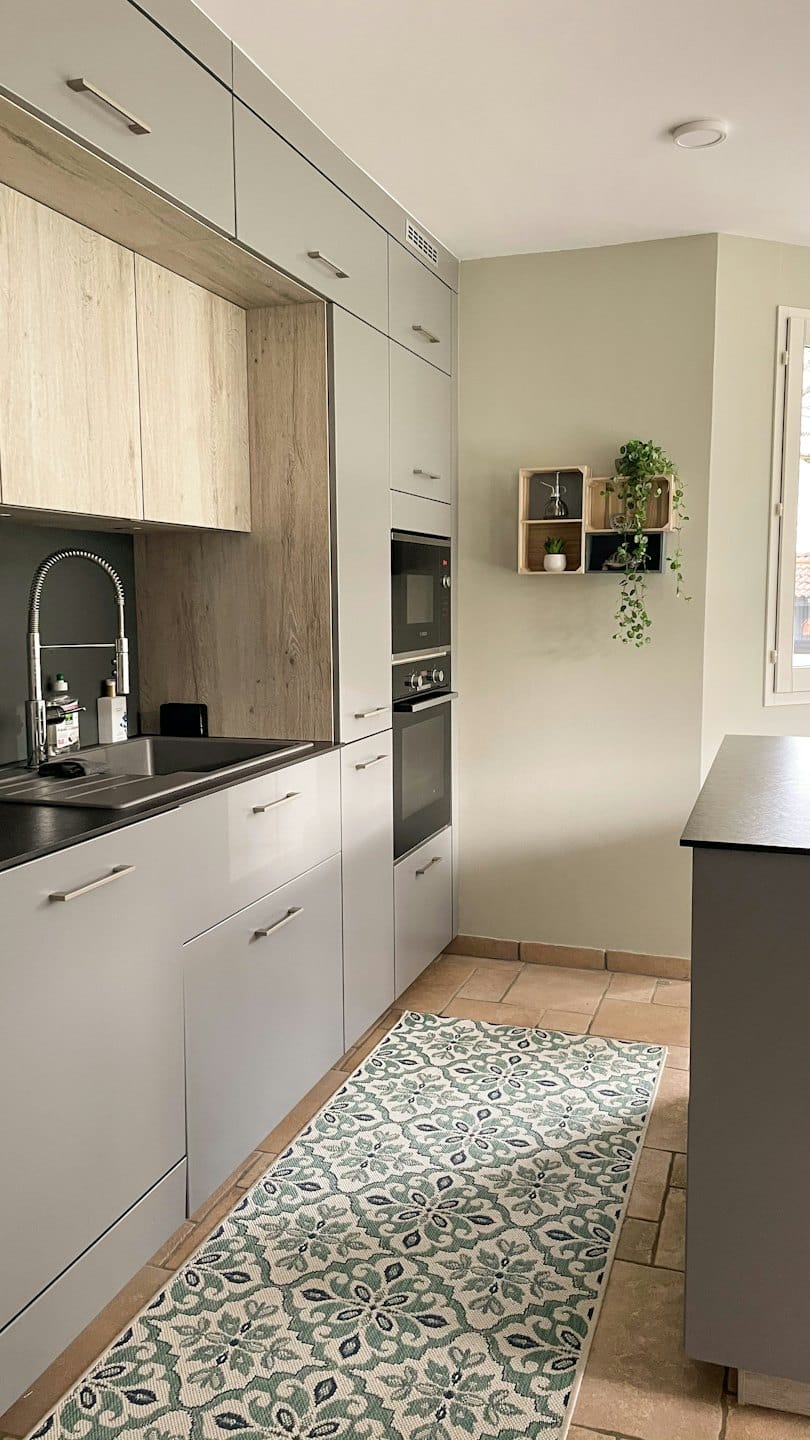 Modern kitchen with grey cabinets, wood accents, and plants on shelves.